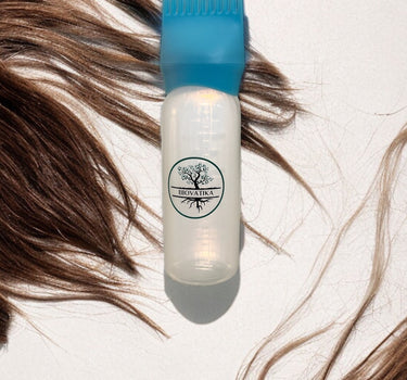 Plastová láhev s nápisem BIOVATIKA Aplikační láhev na vlasy s modrým hřebenovým uzávěrem je umístěna mezi hnědými prameny vlasů na bílé ploše.